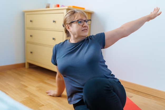 Mulher sênior ativa fazendo exercícios abdominais no tapete de ioga em casa e sorrindo para a câmera