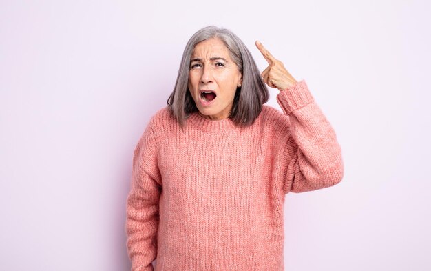 Mulher sênior bonita apontando para a câmera com uma expressão agressiva e zangada, parecendo um chefe louco e furioso