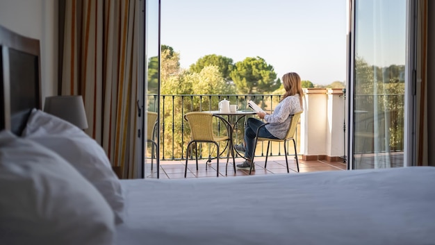 Mulher sênior branca lendo um livro no terraço de seu quarto de hotel de férias