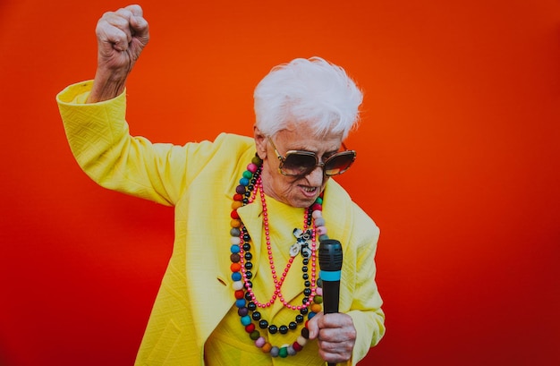 Foto mulher sênior cantando no microfone contra fundo vermelho