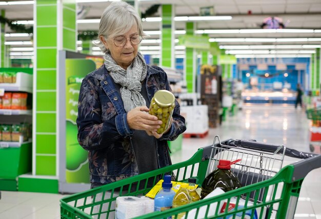 Foto mulher sênior caucasiana fazendo compras no supermercado olhando produtos antes de colocar no carrinho de compras