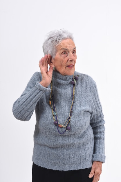 Mulher sênior, colocando uma mão na orelha dela porque ela não consegue ouvir sobre fundo branco