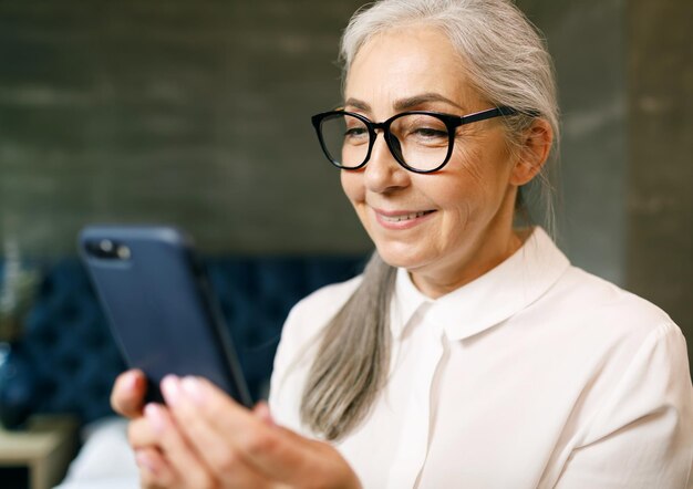 Mulher sênior com cabelos grisalhos em óculos usando smartphone