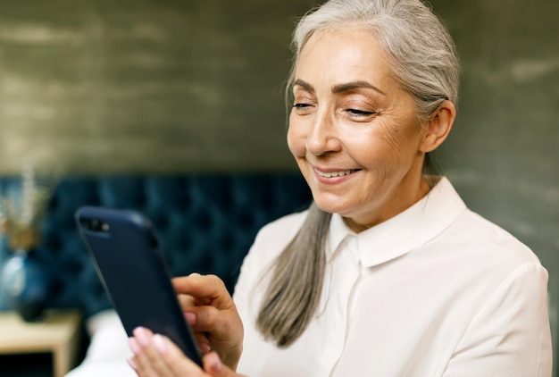 Mulher sênior com cabelos grisalhos segurando smartphone e sorrindo