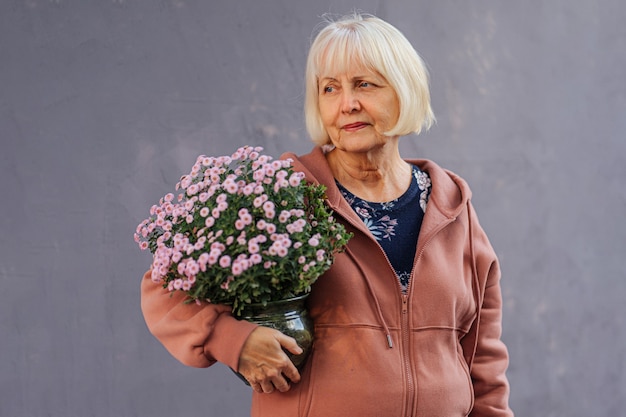 Mulher sênior com flores em vasos. mulher idosa em um moletom da moda carregando um vaso com flores frescas