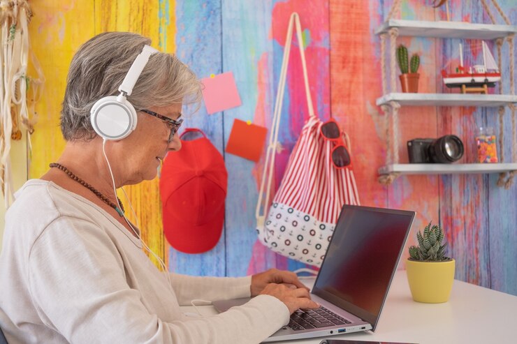 Foto mulher sênior com fones de ouvido, usando o computador portátil. câmera e decoração do mar no fundo