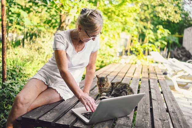 Mulher sênior com gato trabalhando no laptop