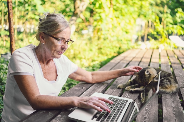 Mulher sênior com gato trabalhando no laptop