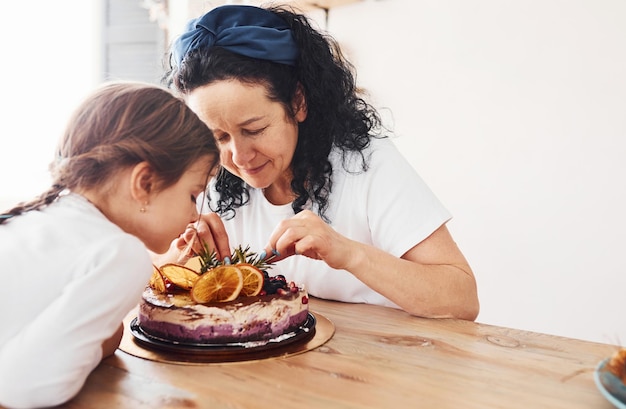 Mulher sênior com sua neta comendo bolo dietético fresco na cozinha