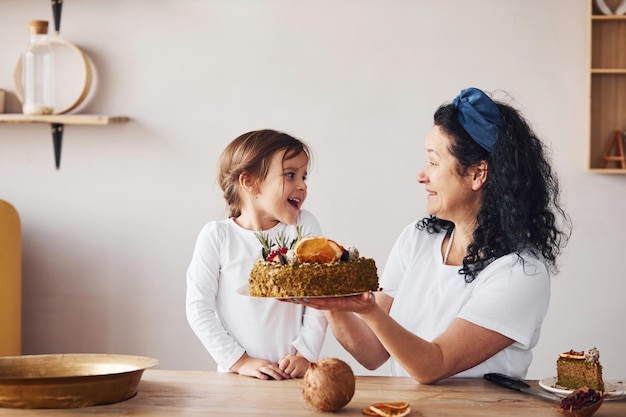 Mulher sênior com sua neta comendo bolo dietético fresco na cozinha