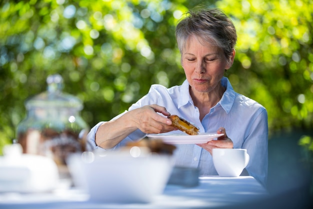 Mulher sênior, comer alimentos doces no jardim