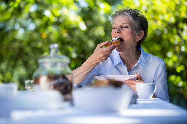 Mulher sênior, comer alimentos doces no jardim