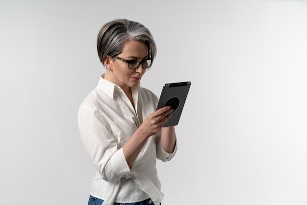 Foto mulher sênior de cabelos grisalhos em camisa branca usando tablet digital. o uso da tecnologia pelos idosos