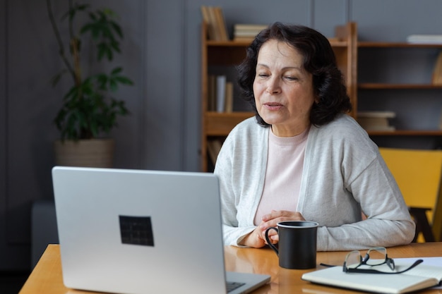 Mulher sênior de meia idade feliz sentada com laptop conversando em videochamada com amigos e família rindo