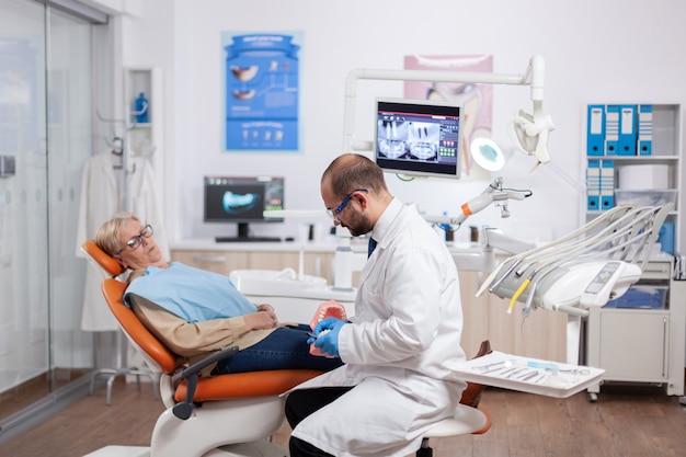 Mulher sênior discutindo com o dentista no gabinete odontológico sobre o problema dos dentes, sentada na cadeira