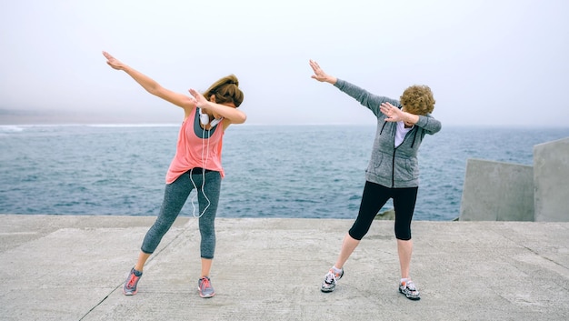 Mulher sênior e jovem fazendo dança dab ao ar livre pelo cais do mar