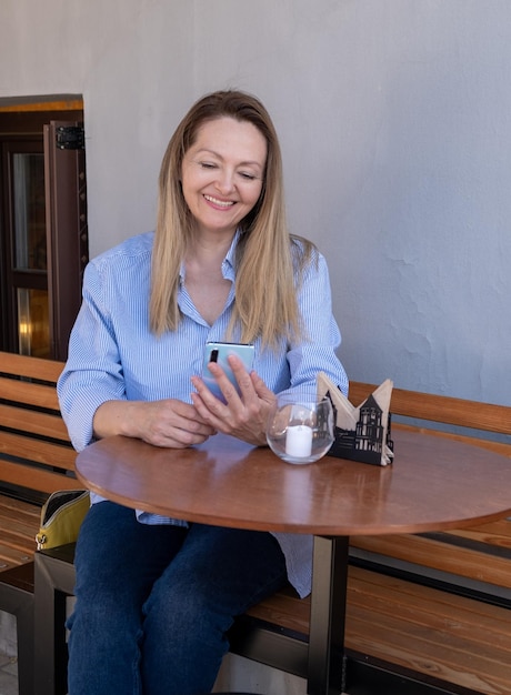 Mulher sênior elegante usando telefone inteligente enquanto está sentado no terraço do café ao ar livre na cidade Conceito de uso de tecnologias modernas por idosos