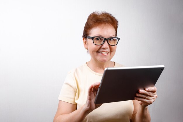 Mulher sênior em copos com um tablet em branco em uma camiseta leve