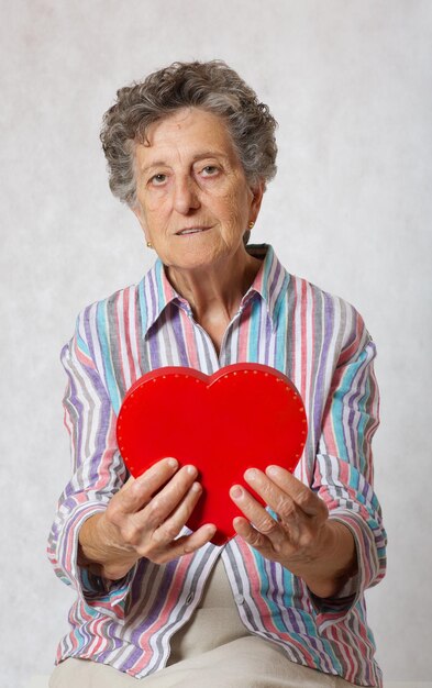 Mulher sênior entre 70 e 80 anos mantém o coração nas mãos. fundo cinza