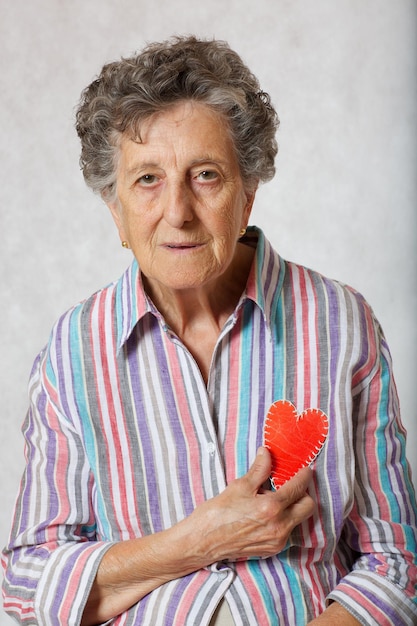Mulher sênior entre 70 e 80 anos mantém o coração nas mãos. fundo cinza