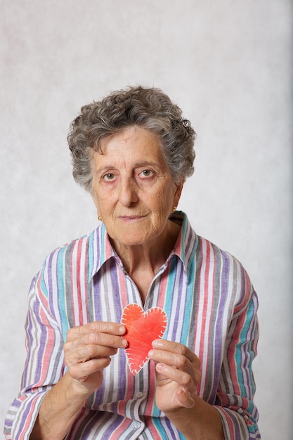Mulher sênior entre 70 e 80 anos mantém o coração nas mãos. fundo cinza