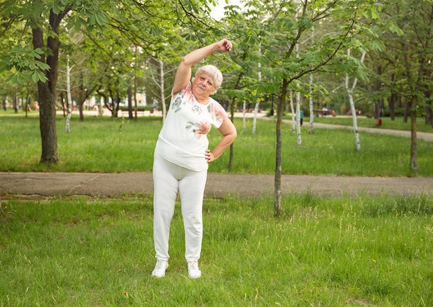 Mulher sênior está fazendo ioga e exercícios de alongamento no parque. Mulher idosa sorridente exercitando-se.