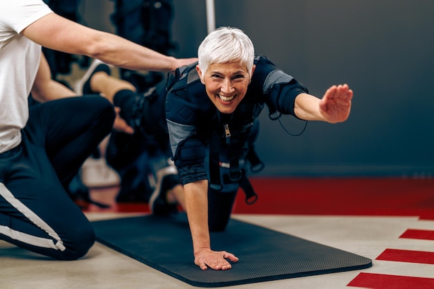 Mulher sênior está fazendo treinamento EMS com personal trainer no ginásio.