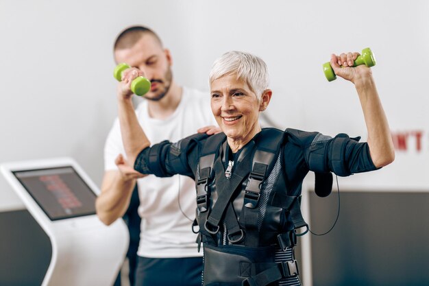 Foto mulher sênior está fazendo treinamento ems com treinador na academia.