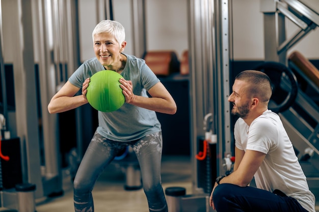 Mulher sênior está treinando com personal trainer no ginásio.