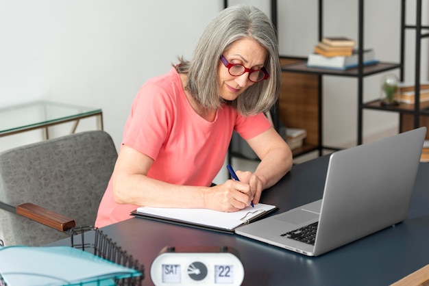 Foto mulher sênior estudando em casa enquanto usa o laptop e faz anotações