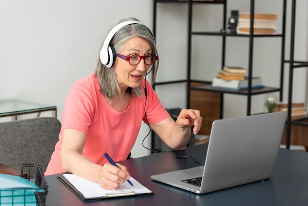 Foto mulher sênior estudando em casa enquanto usa o laptop e faz anotações