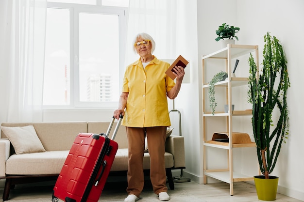 Foto mulher sênior feliz com passaporte e bilhete de viagem embalado uma mala vermelha férias e cuidados de saúde a velha sorridente fica alegremente em casa antes da viagem