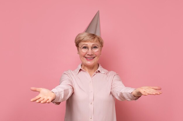 Mulher sênior feliz comemorando e curtindo férias ou festa de aniversário em fundo rosa