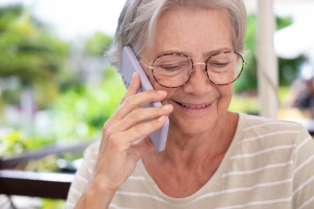 Mulher sênior feliz sentada ao ar livre falando no telefone móvel senhora idosa sorrindo usando telefone