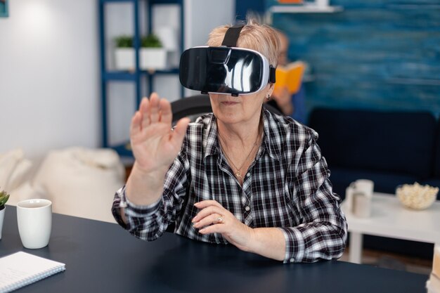 Mulher sênior feliz usando fone de ouvido de realidade virtual e fazendo gestos com a mão