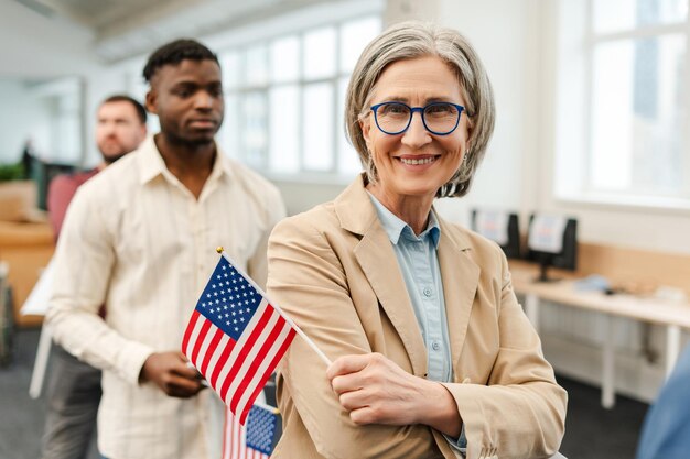 Foto mulher sênior feliz usando óculos elegantes segurando bandeira americana olhando para a câmera em linha