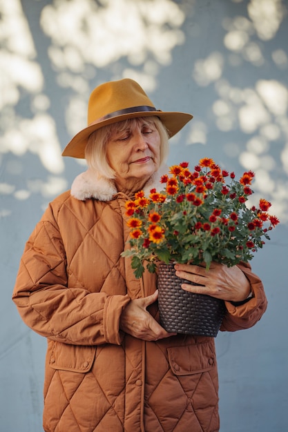 Mulher sênior gosta do perfume das flores. mulher idosa carregando um vaso com flores em um dia ensolarado de verão