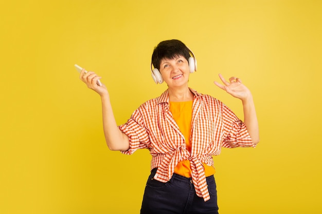 Mulher sênior isolada em fundo amarelo. conceito de estilo de vida de idoso alegre e tecnológico