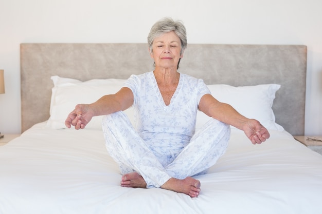 Mulher sênior meditando na cama