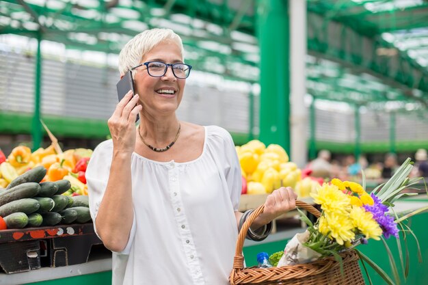 Mulher sênior no mercado usando telefone celular