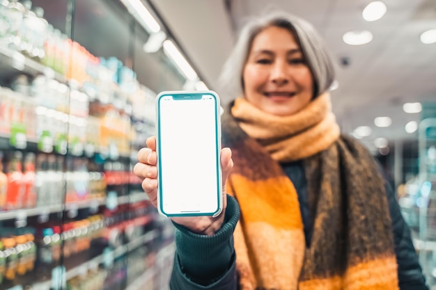 Mulher sênior no supermercado mostra a tela de seu smartphone