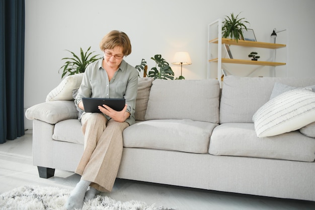 Mulher sênior olhando e rindo de seu tablet digital no sofá