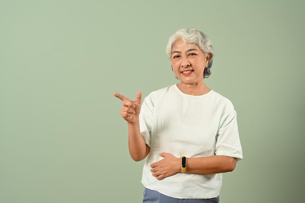 Mulher sênior positiva de 50 anos apontando para o espaço da cópia em fundo azul claro para sua mensagem de texto publicitária
