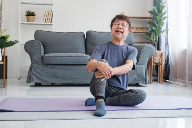 Mulher sênior relaxando e rindo quando terminar de alongar exercícios de ioga na sala de estar em casa