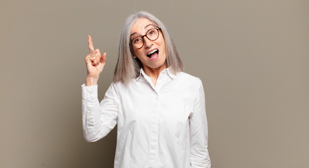 Mulher sênior se sentindo um gênio feliz e animado depois de realizar uma ideia, levantando o dedo alegremente, eureka!