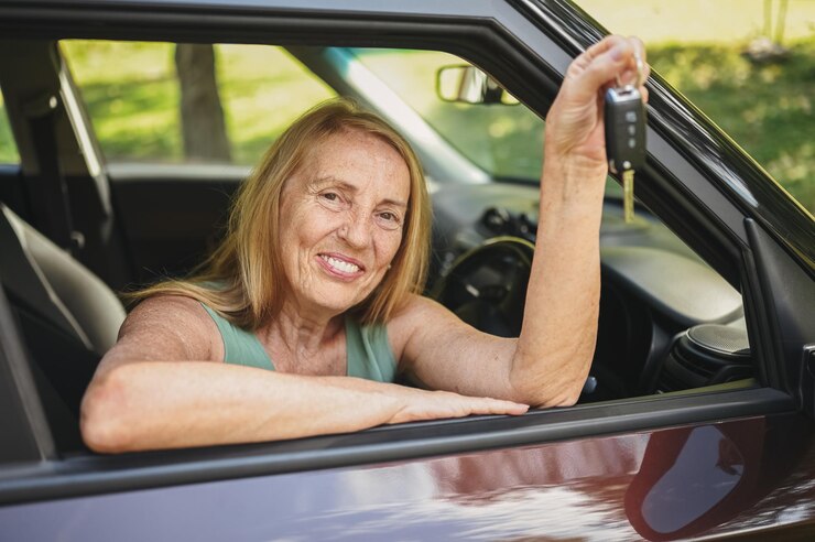 Mulher sênior sentada em um carro novo ao ar livre segurando as chaves sorrindo aproveitando os cursos de condução e