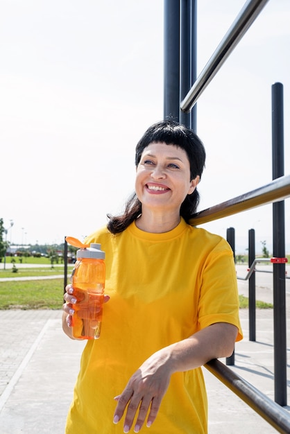 Foto mulher sênior sorridente bebendo água após treino ao ar livre no campo de esportes