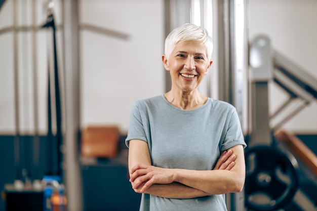 Mulher sênior sorridente está posando após treino no ginásio.