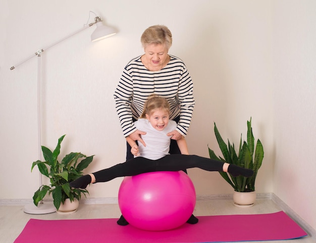 Mulher sênior sorridente fazendo exercícios de alongamento na bola em forma com sua neta Estilo de vida ativo