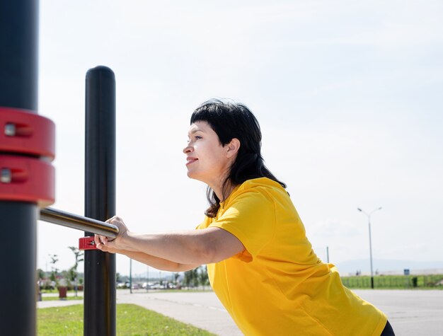 Mulher sênior sorridente fazendo flexões ao ar livre nas barras do campo de esportes